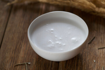 Coconut milk in a bowl on a wooden table. There is dry grass nearby