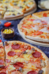Hot tasty traditional various italian pizzas with salami, meat, cheese, onion, mushroom, tomatoes greens on a dark background