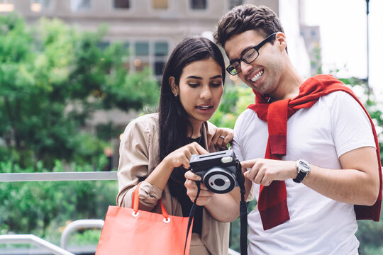Stylish cheerful multiethnic couple using photo camera on street