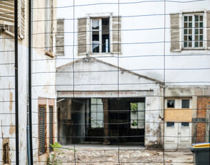 Fototapeta na wymiar An old building glimpsed through a metallic fence, symbolizing the demolition of an old neighborhood