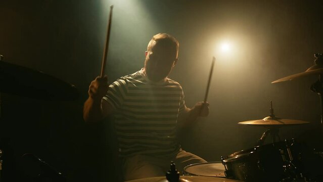 Music band having rehearsal. The drummer emotionally plays drums hitting in a dark room full of smoke