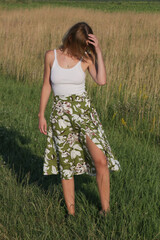 Candid outdoor portrait on the meadow of young woman linen skirt and white top. Casual summer fashion. 