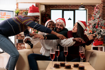 Cheerful coworkers fighting for game console joystick while celebrating christmas in decorated...