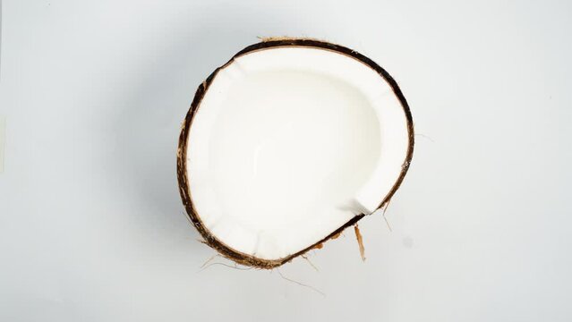 A half of a cracked coconut with white flesh, looped video, on a white background, top-down view.