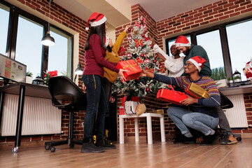 Obraz premium Cheerful happy coworkers sharing christmas gifts while celebrating winter holiday together in office. Diverse company employees preparing for new year party in decorated festive workspace