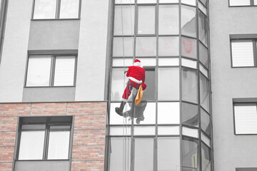 santa descends through the window of a multi-storey apartment building in order to give a gift to a child.