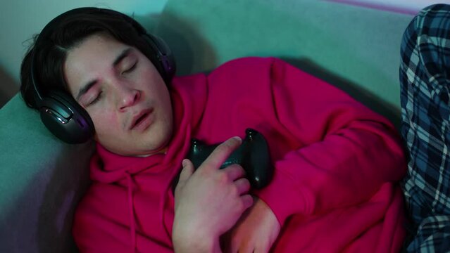 portrait young guy gamer in room falls asleep after playing PS5 with a gamepad