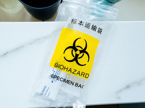 Biohazard yellow sign on a plastic pouch with specimen text in English and Chinese - undergoing COVID-19 test at home