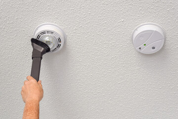 Person's hand vacuuming smoke and carbon monoxide detectors on a ceiling of a domestic room - obrazy, fototapety, plakaty