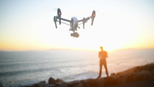 Beach, blurred background and a man flying a drone over the ocean in nature for video footage during summer. Sunset, sea and horizon with a person using a remote to control technology on the coast