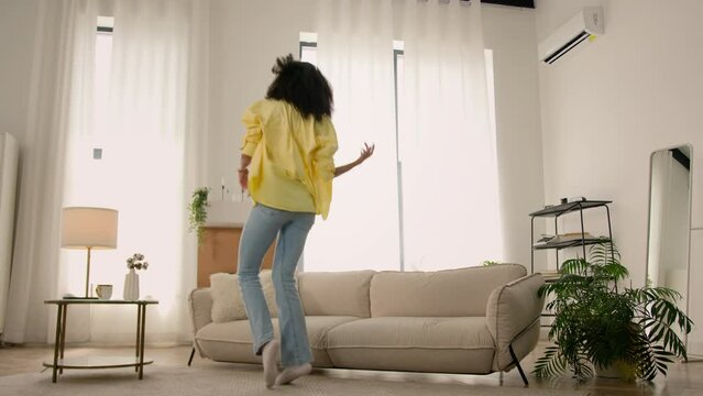 Happy joyful crazy African American woman girl real estate owner homeowner rejoice jump in cozy living room good mood joy dancing active motion fun energy dance to music home funny party free weekend