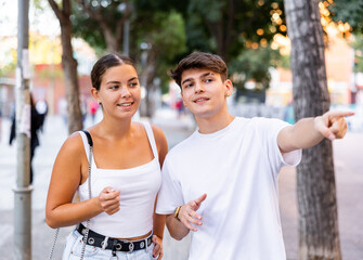 Young man and woman walking through city streets together, pointing finger to show direction.