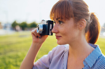 redhead hipster girl photographer spending free time on hobby making photos on sunny day