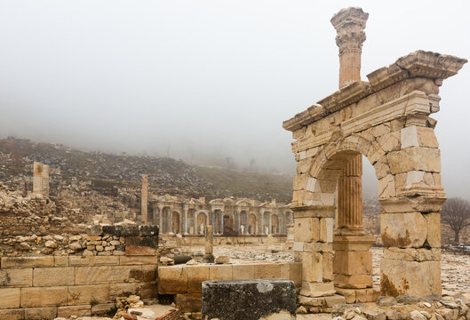 Reconstructed arched honorific emperor gates and column on ancient street of Pisidian town of Sagalassos in foggy winter day, Turkey..