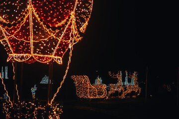  Christmas installation.Glowing balloon,reindeer with sleigh made of garlands. Festive Christmas street decoration.Light installation made of garlands.