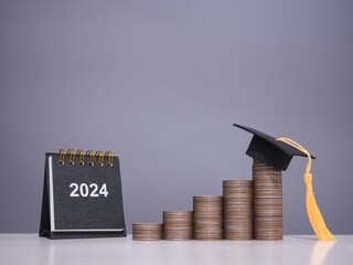 Study goals, 2024 Desk calendar, Graduation hat on stack of coins. The concept of saving money for education, student loan, scholarship, tuition fees in New Year 2024 - obrazy, fototapety, plakaty