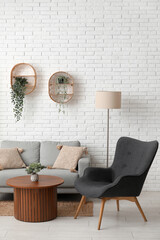 Couch with armchair, wooden coffee table and houseplants near white brick wall