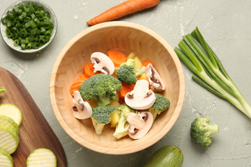 Bowl with fresh vegetables on grey background