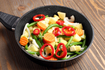 Frying pan with fresh vegetables on wooden background