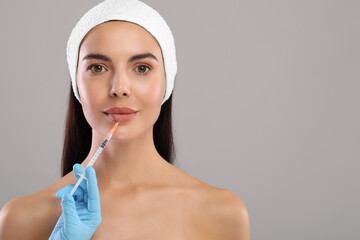 Doctor giving lips injection to young woman on light grey background, space for text. Cosmetic...