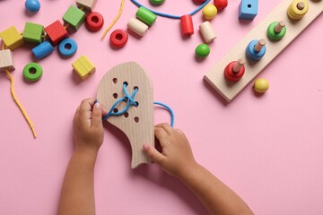 Motor skills development. Little child playing with wooden lacing toy at pink table, top view