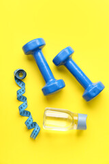 Dumbbells, measuring tape and bottle of water on color background