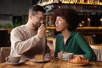 Fototapeta na wymiar International dating. Handsome man feeding his girlfriend with cake in cafe