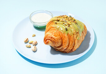 Plate with sweet croissant and pistachio nuts on blue background