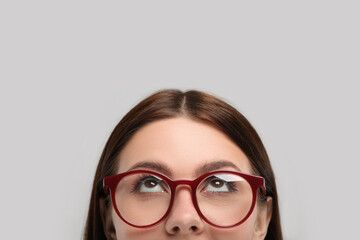Woman in stylish eyeglasses looking up on grey background, closeup. Space for text