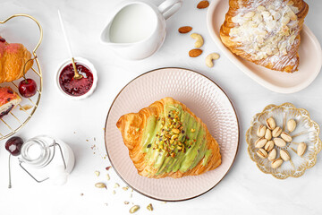 Composition with tasty croissants, pistachio nuts, jam and milk on light background