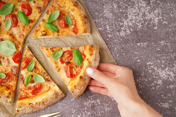 Woman taking piece of tasty pizza Margarita with tomatoes and basil on dark table