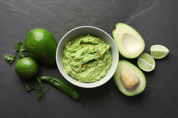 Delicious guacamole, fresh avocado and parsley on dark grey table, flat lay
