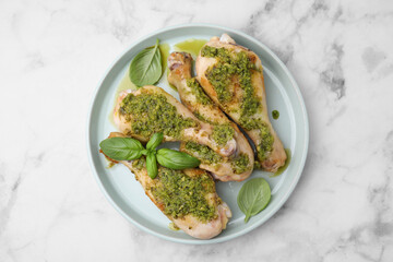 Delicious fried chicken drumsticks with pesto sauce and basil on white marble table, top view