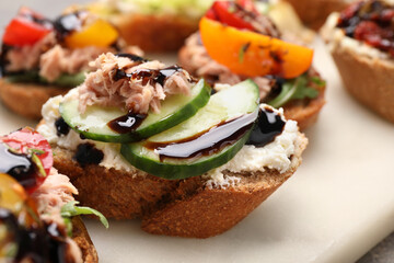 Delicious bruschettas with balsamic vinegar and different toppings on white board, closeup