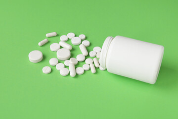 Jar with scattered pills on green background