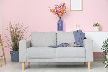 Interior of stylish living room with grey sofa, houseplants and flowers