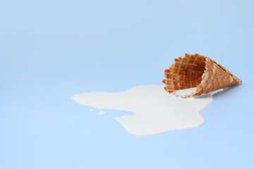 Melted ice cream and wafer cone on light blue background, space for text