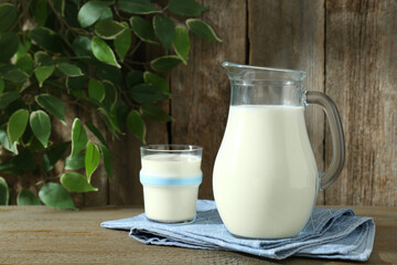 Jug and glass of fresh milk on wooden table, space for text