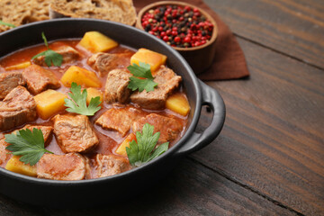 Delicious goulash in pot on wooden table, closeup. Space for text