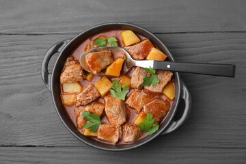 Delicious goulash in pot on dark wooden table, top view