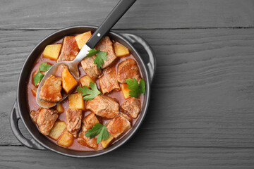 Delicious goulash in pot on dark wooden table, top view. Space for text