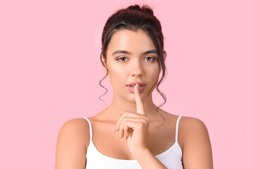 Fototapeta premium Young woman with beautiful lips showing silence gesture on pink background, closeup