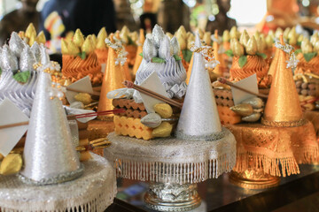 Gold rice offering with flower tray, incense, candles on golden stand for ordination ceremony of Buddhist temple in Thailand.