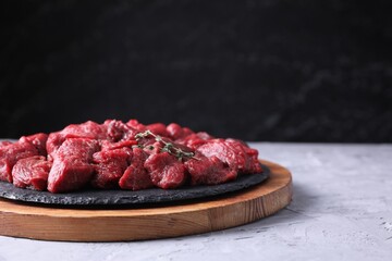 Pieces of raw beef meat and thyme sprigs on grey textured table against black background. Space for...