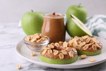 Fresh green apples with peanut butter and nuts on white marble table, closeup