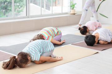 Group of little children practicing yoga with instructor in gym