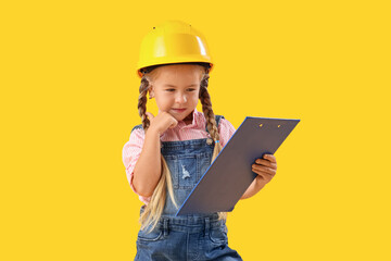 Cute little builder girl with clipboard on yellow background