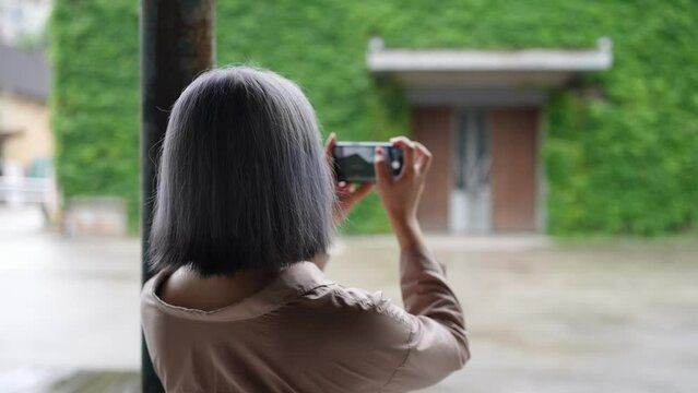 台北の華山1914文創園区の芸術的な建物でスマートフォンで撮影している若い台湾人女性 A young Taiwanese woman takes a picture with her smartphone at an artistic building in the Huashan 1914 Cultural and Creative Park in Taipei.