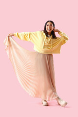 Young Asian woman in yellow hoodie on pink background