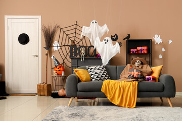 Scary Halloween skeleton in autumn clothes with gift box and tarantula sitting on sofa in living...